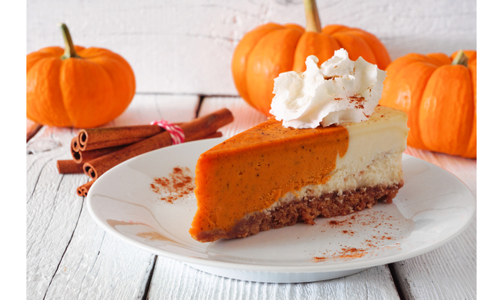 Slice of pumpkin pie cheesecake with whipped cream, side view table scene against white wood