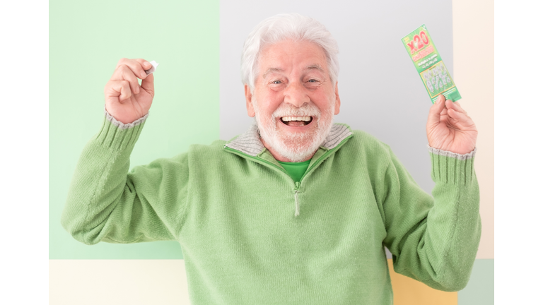 Happy caucasian white-haired senior man doesn't believe his eyes holding filled winning lottery ticket and celebrating victory. Lucky excited smiling mature man won a jackpot.