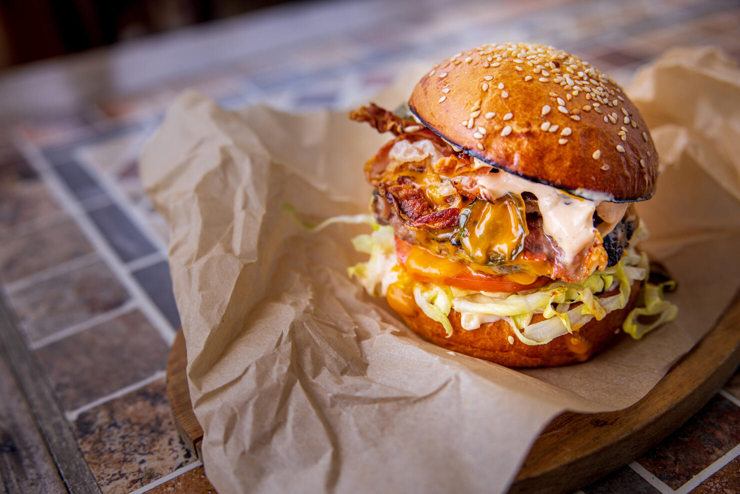 Bacon cheeseburger with salad in bun, served on wooden board