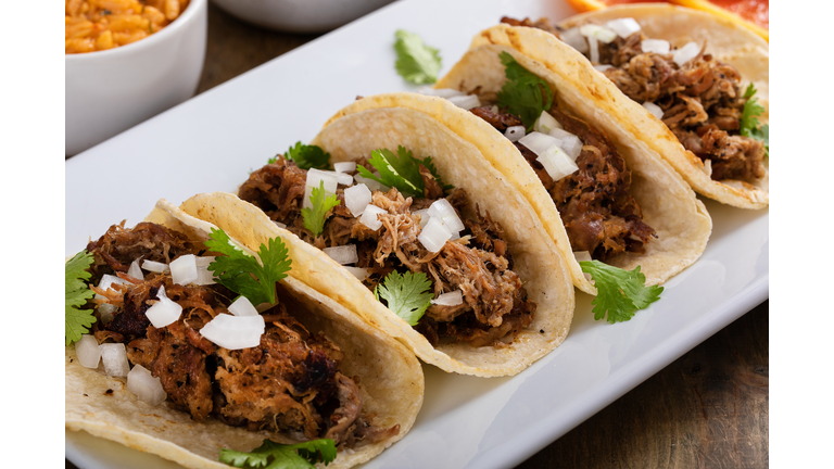 Pork carnitas tacos on corn tortillas with rice and beans