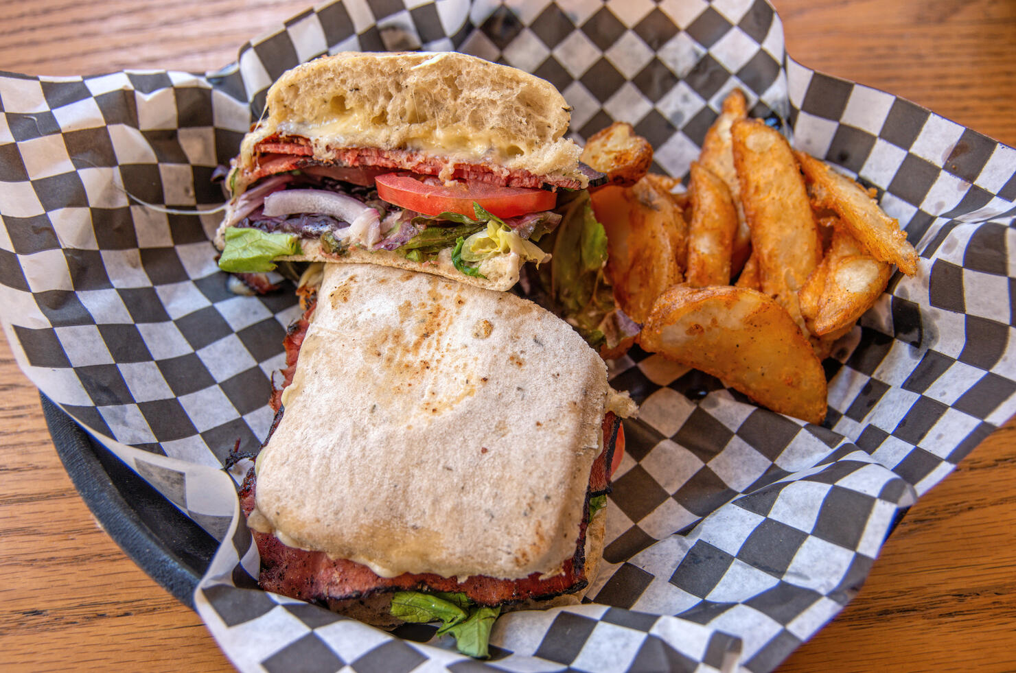 Roast beef panini with a side of potato wedges in a greaseproof paper lined serving basket