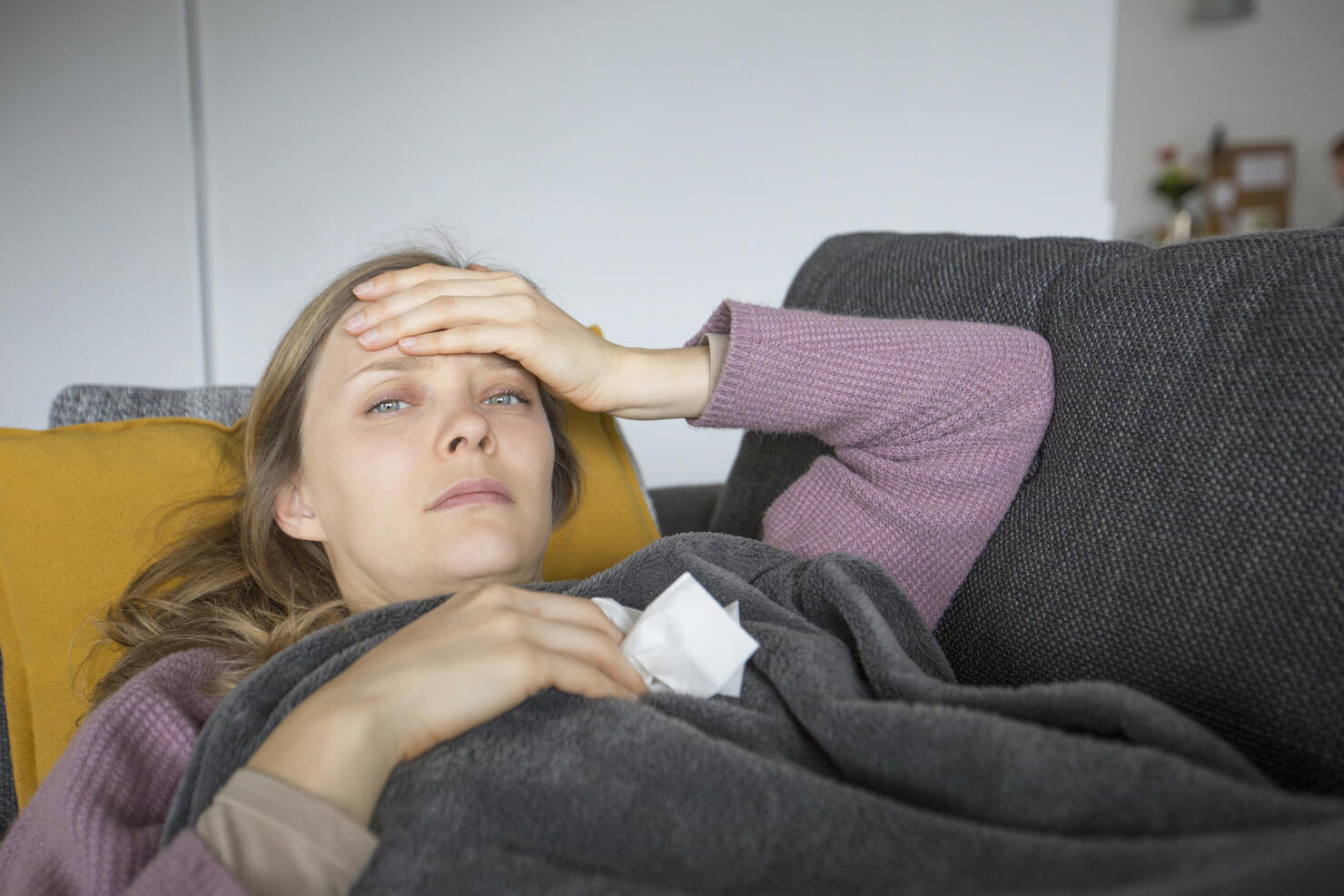 Sick woman holding one hand on head, having napkin in another