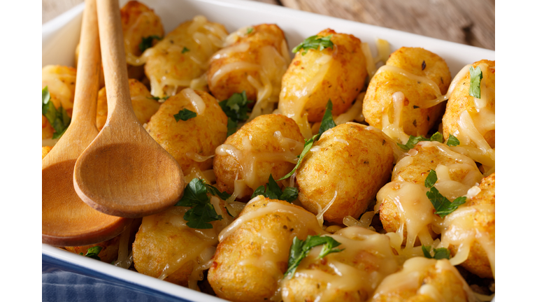 Baked Tater Tots with cheese and herbs close up in a dish baking dish. horizontal