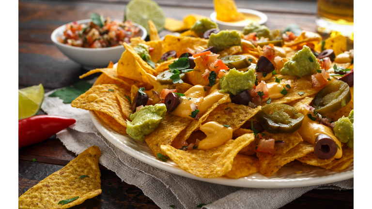 Mexican nachos tortilla chips with olives, jalapeno, guacamole, tomatoes salsa, cheese dipand beer.