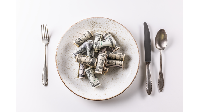 American dollar bills on a plate with cutlery on a white background