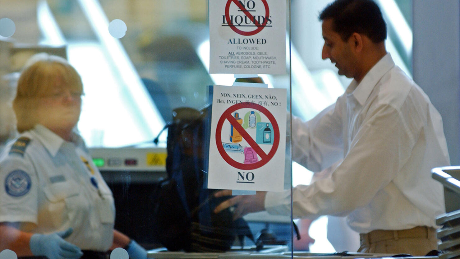Passengers line up at a security check point displaying sign