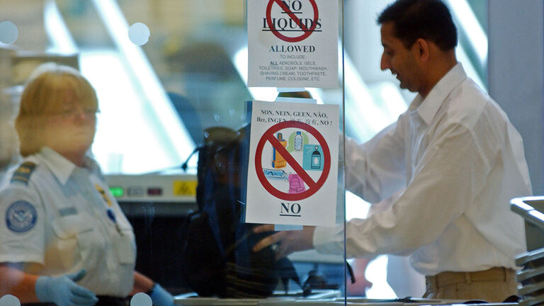 Passengers line up at a security check point displaying sign
