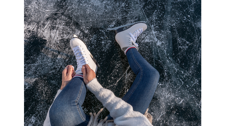 Young woman on frozen lake putting on ice skates at sunset getting ready to have fun and enjoy winter vacations