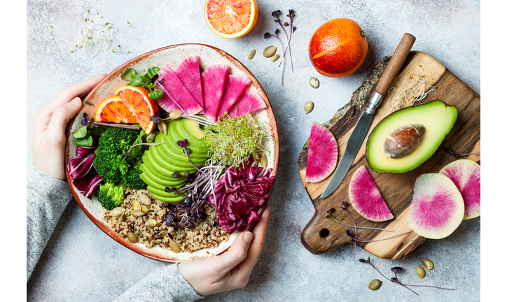 Girl holding vegan, detox Buddha bowl with quinoa, micro greens, avocado, blood orange, broccoli, watermelon radish, alfalfa seed sprouts.