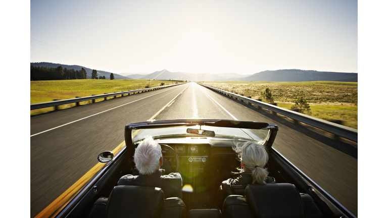 Senior couple driving convertible car at sunrise