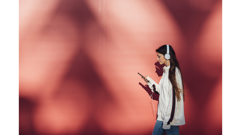 Teenage girl using mobile phone while walking by red wall