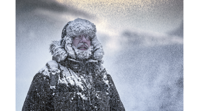 Wintery scene of a man with Furry and full beard shivering in a snow storm
