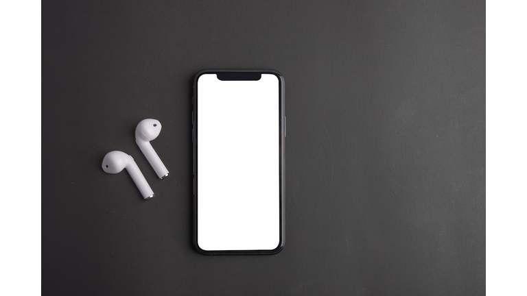 White wireless bluetooth earphones or headphones and smartphone over black background. Close up. Copy space.