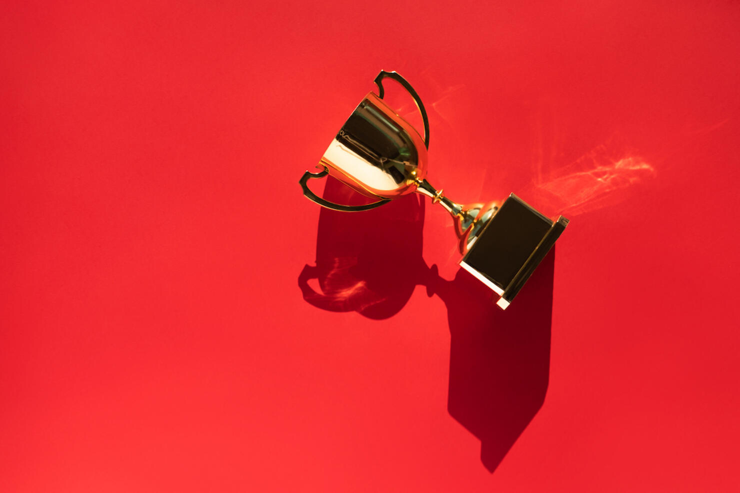 Top view of metallic golden goblet on bright red background with shadow. Goal achievement concept. Trendy colors of the year