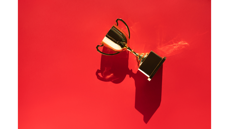 Top view of metallic golden goblet on bright red background with shadow. Goal achievement concept. Trendy colors of the year