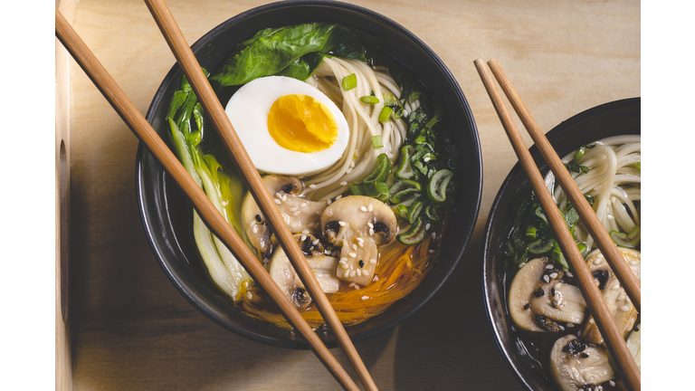 Traditional japanese Ramen soup with  mushrooms, Bok Choy, greens in  two black bowls on the orange background, top view, close up