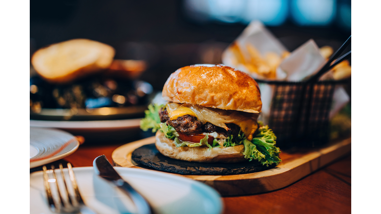 Fresh delicious burger with french fries and salad served on rustic wooden board on table. A feast on the dining table in restaurant. Food and lifestyle concept