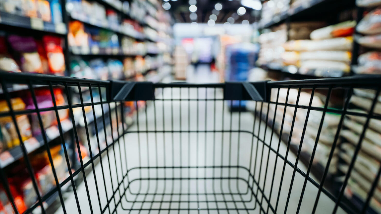 Personal perspective of a shopper pushing shopping trolley along product aisle while shopping in a supermarket