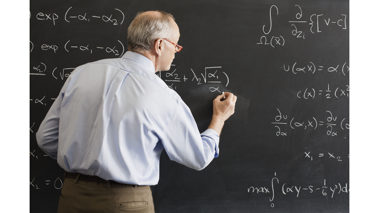Teacher writing algebra equation on chalkboard