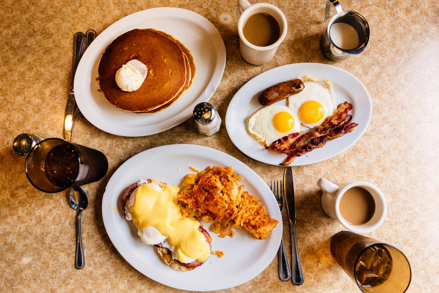 Pancakes, fried eggs with bacon and Eggs Benedict with ham and hash brown served at a traditional American diner, high angle view