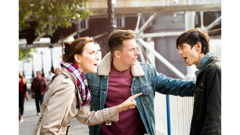 Two women fighting each other while man keeps them apart