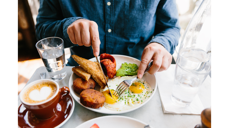 Man eating breakfast with fried eggs, hash brown, avocado, sausage and toasted bread