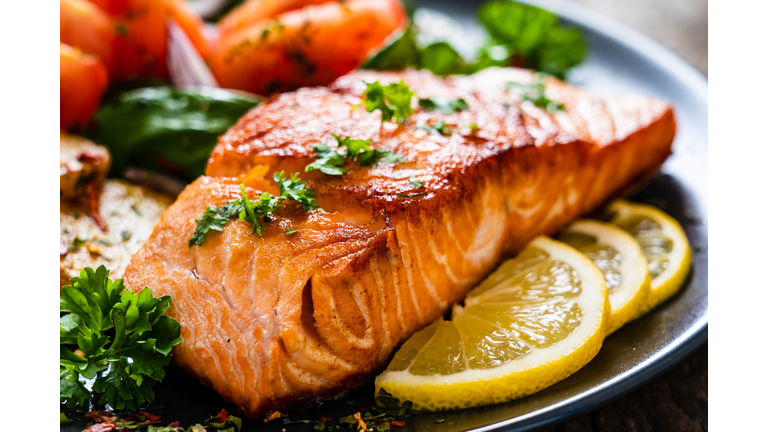 Barbecued salmon, fried potatoes and vegetables on wooden background