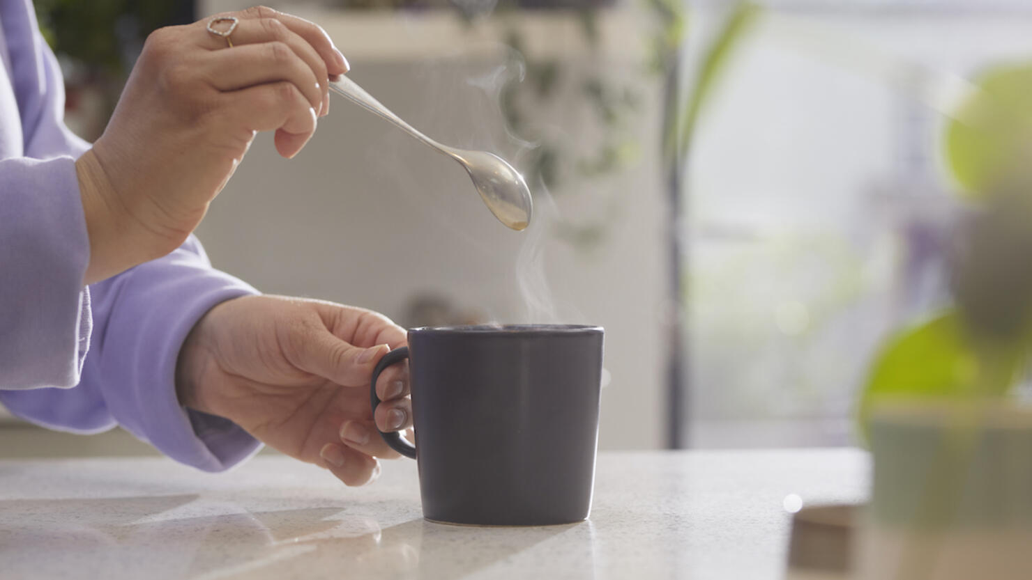 Close up of hands holding spoon after stirring a hot drink in a mug