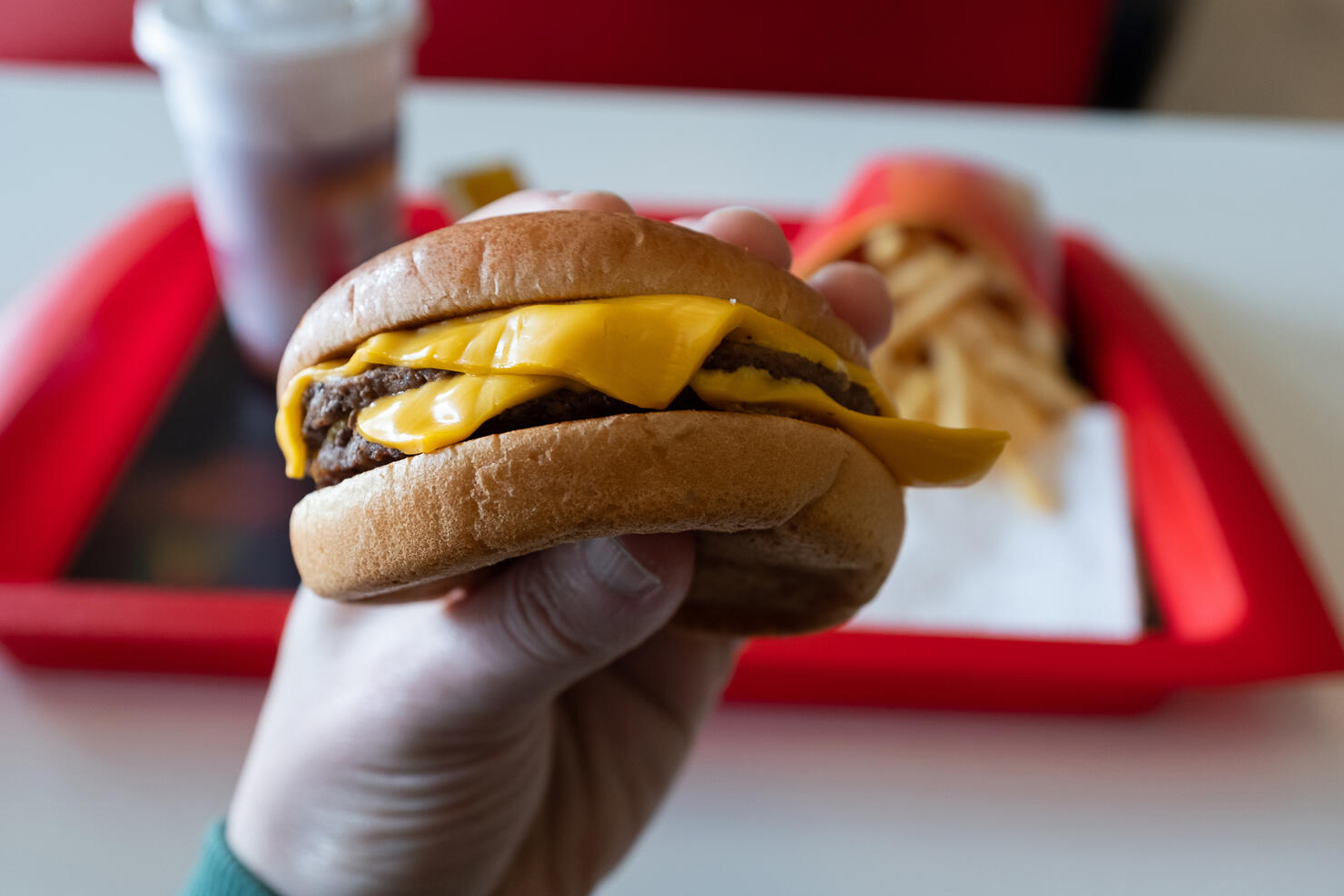A young man is holding a piece of hamburger in his hands. A guy or a man eats fast food. A hungry skinny guy is eating an appetizing burger. The concept of unhealthy food, diet, overeating, gluttony, dependence on food. Fast food restaurant, snack bar.