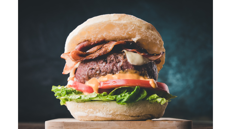 View of fresh tasty burger on wooden table. Hamburger with bacon, cheese, lettuce, tomato and sauce