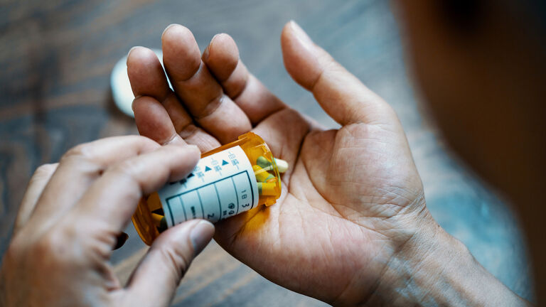 Close-up of a male hand holding a pill bottle pouring medication into his hand