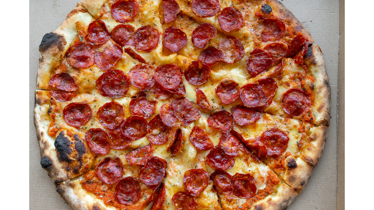 Delicious Italian pizza in a pizza box and a delivery box, on the table in a pizzeria. Sliced pizza slice with tomatoes, pepperoni sausage and cheese. The concept of unhealthy lifestyle, overeating, junk food, fast food. Delivery to your home or work.