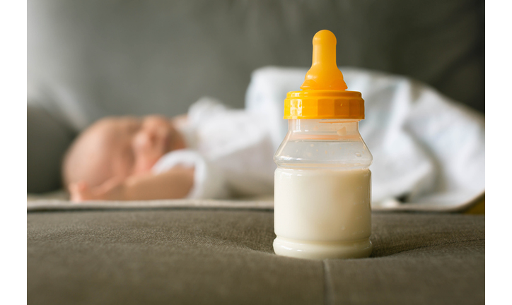 A bottle of milk and a baby sleeping. Formula milk feeding and sleep schedule for infants.