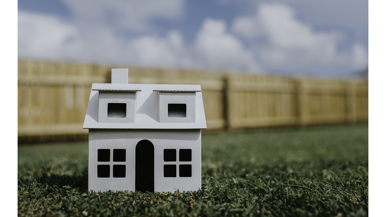 Conceptual image of a plain, white, cardboard house outside on grass