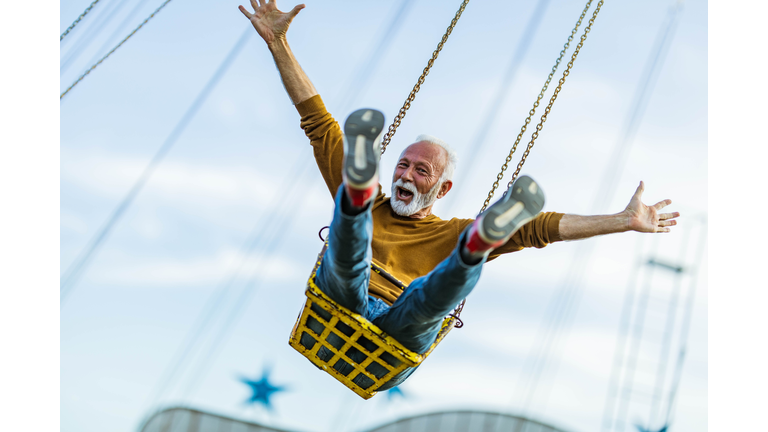 Carefree mature man having fun on chain swing ride in amusement park.