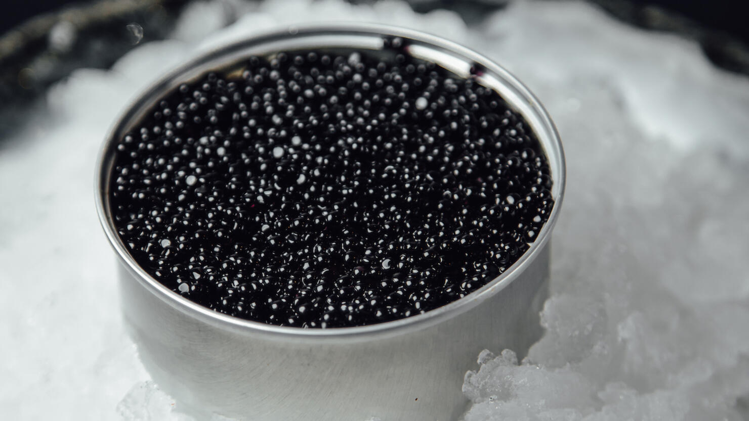 black caviar in a silver jar on ice on a dark background