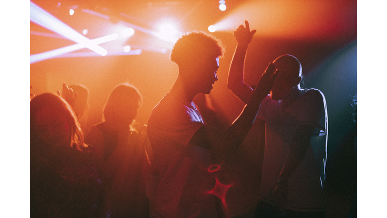 Young men and women dancing against illuminated red spotlights at nightclub