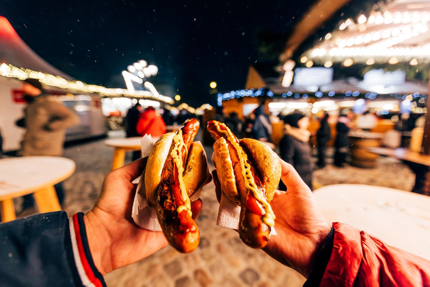 Friends eating bratwurst sausage with mustard and ketchup at Christmas market in Berlin, Germany