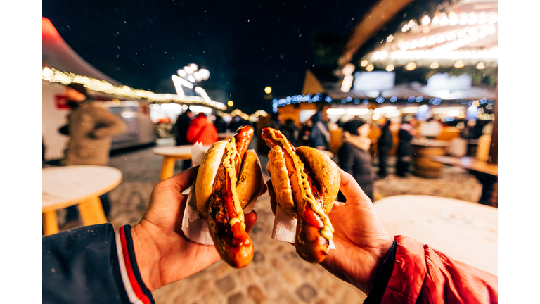 Friends eating bratwurst sausage with mustard and ketchup at Christmas market in Berlin, Germany