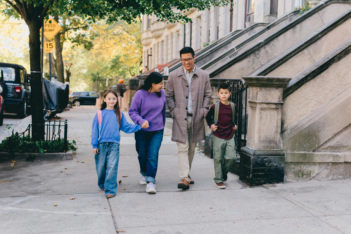 A family of four is walking down the sidewalk in the morning as they make their way home from school and work