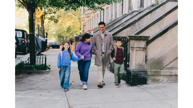 A family of four is walking down the sidewalk in the morning as they make their way home from school and work