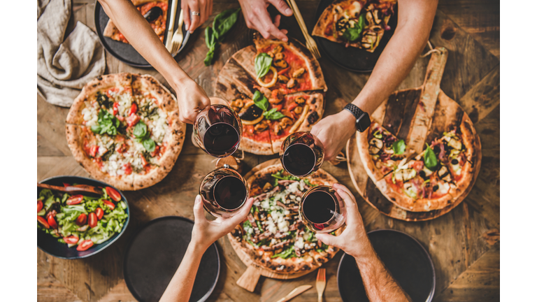 People clinking glasses with wine over table with Italian pizza