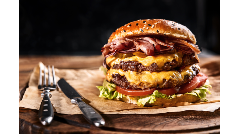 Fresh and juicy hamburger on a paper pillow with beer on a wooden table. Dark background, traditional american food. Junk food