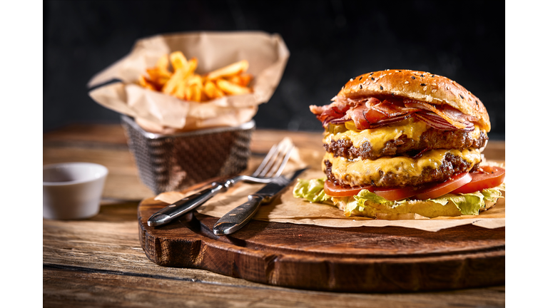 Juicy burger on the board, black background. Dark background, fast food. Traditional american food. Copy space