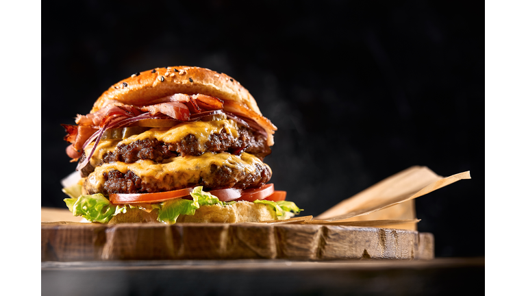 Juicy burger on the board, black background. Dark background, fast food. Traditional american food. Copy space