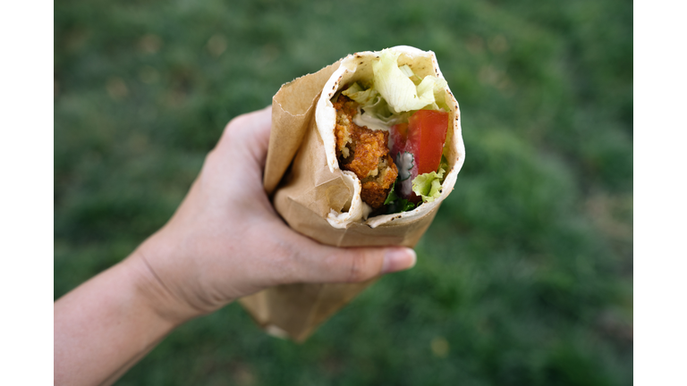 Falafel wrap in female hand held oudoors. Vegan street food concept.