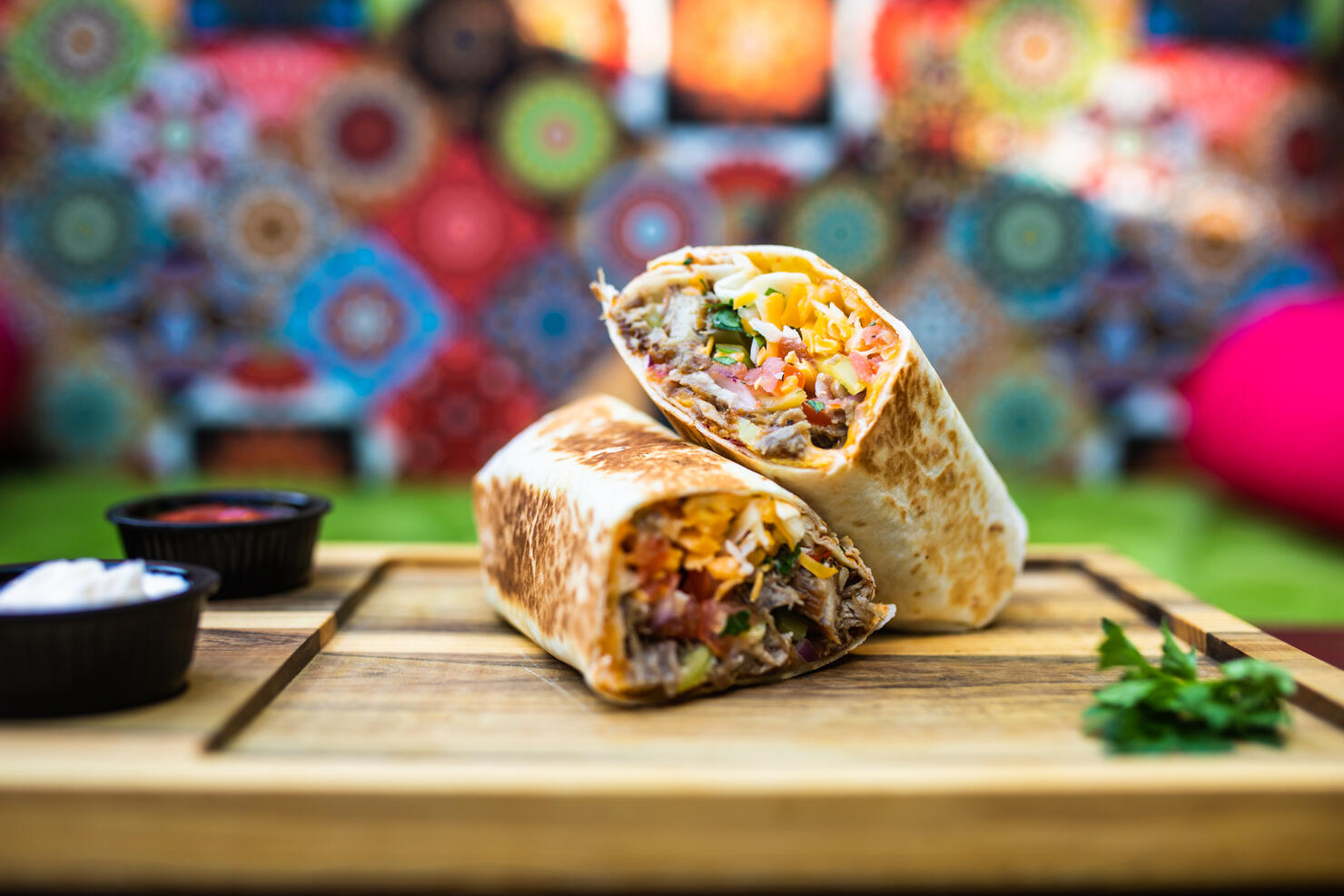 A burrito with dips cut in half on a wooden board