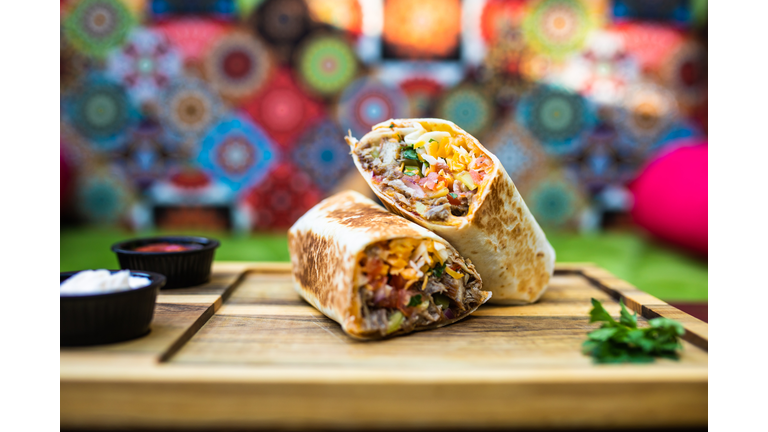 A burrito with dips cut in half on a wooden board