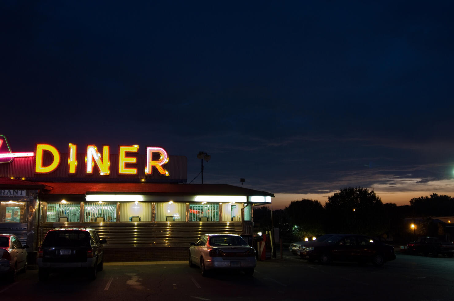 A diner sign lit up at night with cars parked