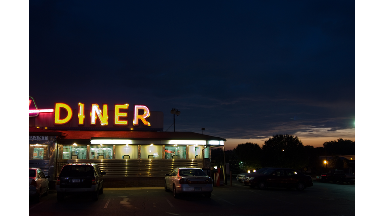 A diner sign lit up at night with cars parked
